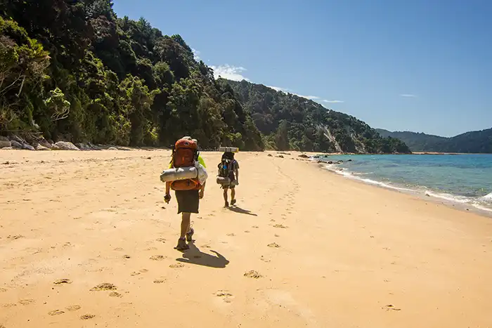  Two trampers walk along an empty gold sand beach on the Abel Tasman National Park