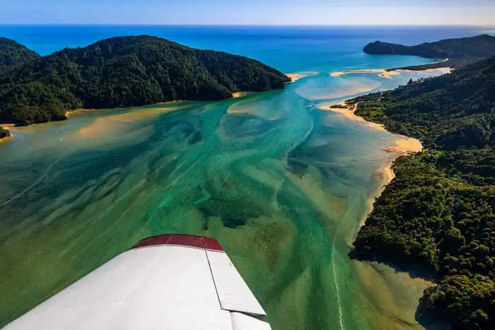 Scenic flight view of Awaroa Inlet, Abel Tasman, emerald green water patterns in the estuary contrast with the golden beaches and green forrest lapping at the water