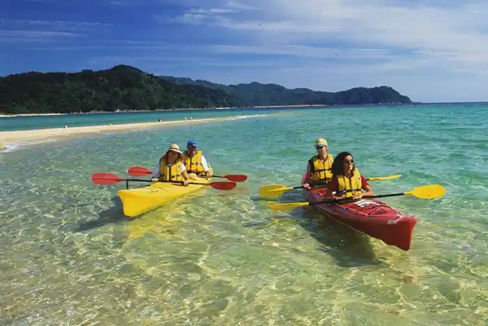 Kayakers drift in clear shallow water near a golden sand beach in the Abel Tasman National Park