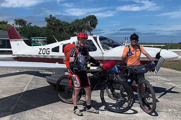 Two bikers pose with their bikes in front of Golden Bay Air Piper Archer at Karamea Aerodrome