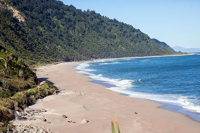 A lone rider heads off along the expansive Heaphy coastline, blue sky and forest to the edge of the beach