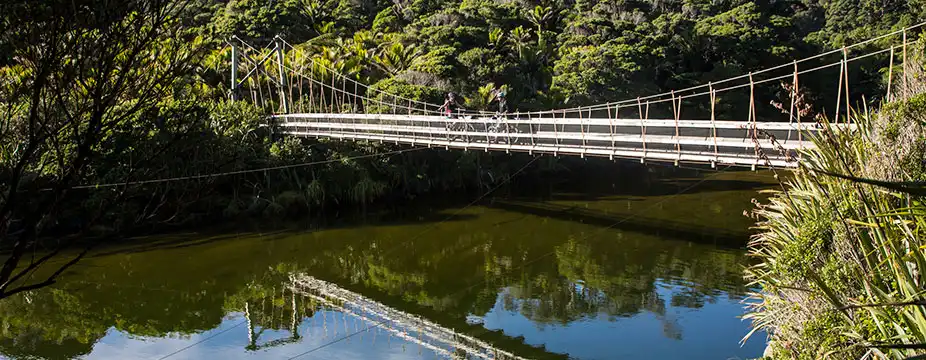  Two riders pose on the swing bridge over the Kohaihai river, at the start of the Heaphy Track, their image reflected in the water