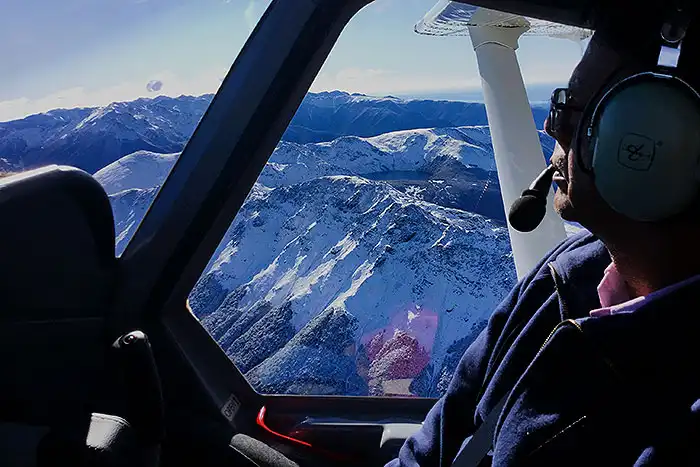 Passenger wearing headset looking out window of aircraft over snowy mountains of Kahurangi National Park