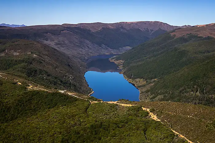 Aerial view of Cobb Reservoir, perfectly flat water reflecting surrounding ridges of Kahurangi National Park